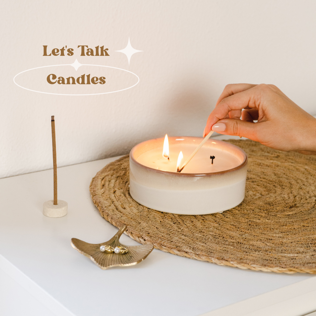 Image shows a candle in a pretty ceramic vessel on a pretty table with a brass jewelry dish. The candle is being lit and has words in upper left corner "let's talk: candles"